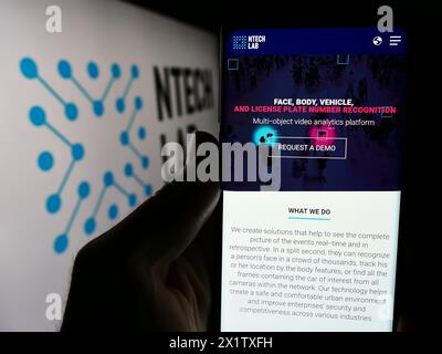 Person holding smartphone with webpage of Russian facial recognition company NtechLab (Findface) with logo. Focus on center of phone display. Stock Photo