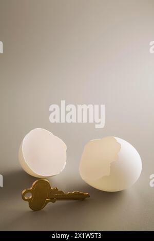 Close-up of antique brass key and two white cracked opened chicken egg shells on grey background, Studio Composition, Quebec, Canada Stock Photo