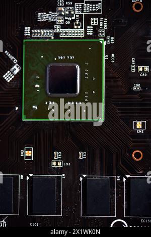 A brown printed circuit board with a processor chip and video memory strips. Electronic components on the graphics card. Stock Photo
