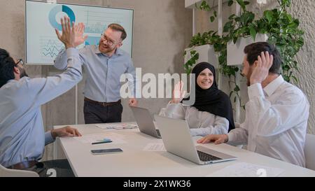 Happy team colleagues celebrate winning business deal achieve victory give high five multiethnic businessmen and muslim businesswoman in hijab working Stock Photo