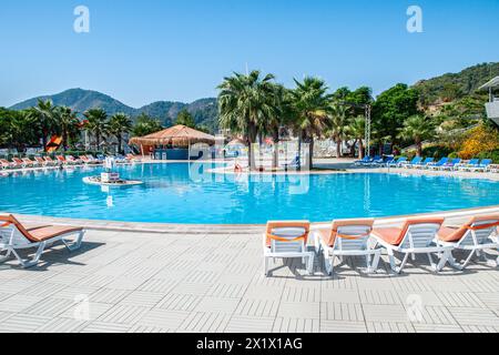 Circular swimming pool surrounded by lounge chairs and a bar with a thatched roof, in a summer water park in the early morning Stock Photo