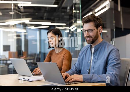 Adult couple in casual clothes working with computers and looking at screens while using keyboard. Couple of freelancers visiting shared office area for creating productive atmosphere out of home. Stock Photo