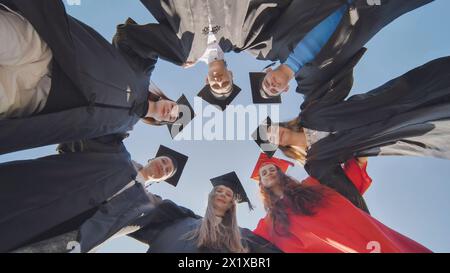 College graduates in a circle stand hugging each other. Stock Photo