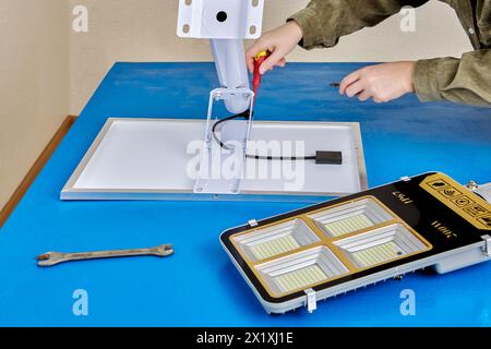 Assembling stand alone solar street light, an electrician attaches solar module and LED luminary to light arm or mounting bracket. Stock Photo