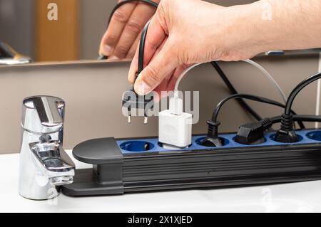 Close up of a woman hand plugging a plug in an electrical socket at bathroom Stock Photo