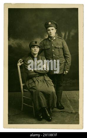 Original WW1 era postcard portrati of women's army auxiliary corps  (W.A.A.C.) recruit wearing a standard issue trench coat, cap, maybe a driver seated, with Canadian army boyfriend, who wears a cap with a maple leaf badge. The W.A.A.C. was founded 1917 so this image dates from this period in the Great War. Stock Photo