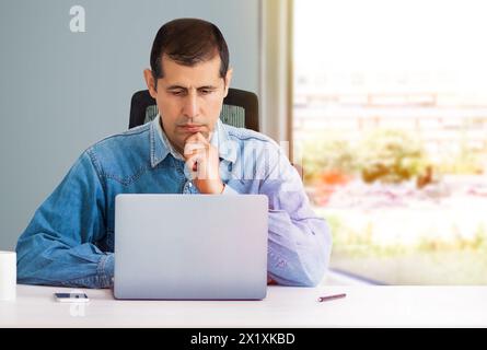 Cropped shot of a handsome young businessman looking thoughtful while working on his laptop in the office Stock Photo