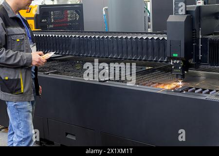 A worker operates a steel laser cutting machine at a factory. Industry Stock Photo
