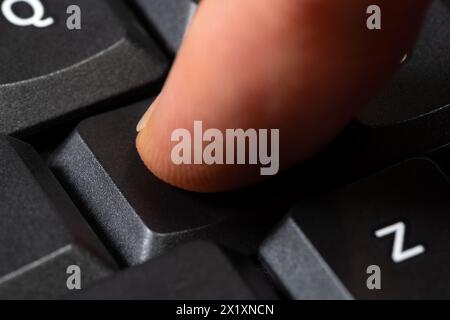 Close-up shot of a finger mid-action as it presses an unlabeled black key on a modern computer keyboard. Taking action, any key button press, anonymou Stock Photo