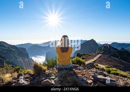 Description: A female toruist sits on the top of a mountain and enjoys the panoramic view over a volcanic island on a sunny summer afternoon. Pico do Stock Photo