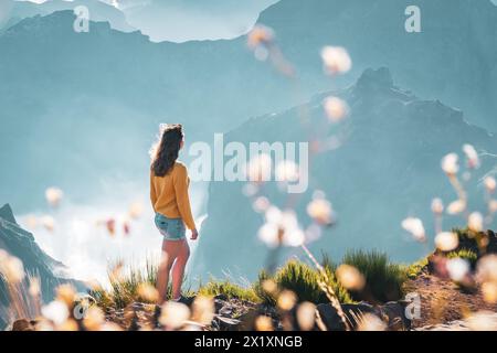 Description: Female toruist stands on the windy edge of a deep, cloud-covered valley and enjoys the breathtaking panoramic view of the volcanic mounta Stock Photo