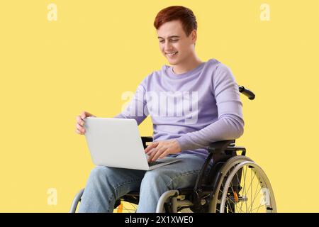 Young man in wheelchair using laptop on yellow background Stock Photo