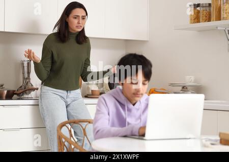 Unhappy mother and her son using laptop in kitchen. Family problem concept Stock Photo