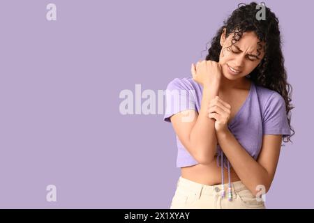 Young African-American woman with skin allergy scratching herself on lilac background Stock Photo