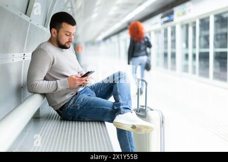 Bearded traveler with phone waiting for train on bench at metro station Stock Photo