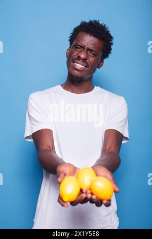 African american person holding lemons for healthy vegetarian diet. Man presenting yellow citrus fruits in hands for natural nutrition with vitamins. Adult showing fresh juicy fruits to camera. Stock Photo