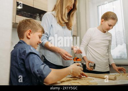 A woman and two boys are gathered around a kitchen counter, mixing ingredients and shaping dough to make cookies together. Stock Photo