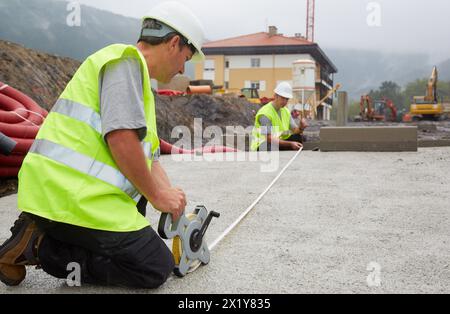 Workers with protective equipment, PPE, Taking measures in urbanization, Outside, Housing construction, Measuring tape, Basque Country, Spain. Stock Photo