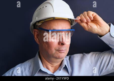 elderly male engineer, builder in protective helmet, glasses looking seriously, modern architecture concept, real estate purchase consultation Stock Photo