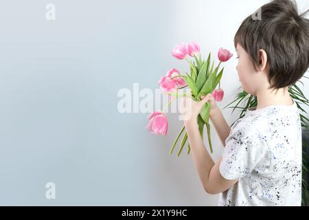 child, boy 8-10 years old holding a bouquet of pink tulips in his hands, the concept of giving fresh flowers, mother's day, birthday, gratitude Stock Photo