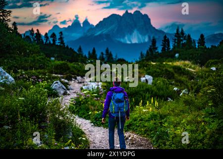 Description: Athletic woman walks on hiking trail at Sorapis lake with impressive view on Cadini di Misurina in the background in the evening. Lake So Stock Photo