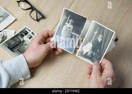 closeup male hand holding old vintage photos of 1940-1950, glasses on the table, concept of family tree, genealogy, childhood memories, memory of ance Stock Photo