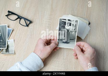 closeup male hand holding old vintage photos of 1940-1950, glasses on the table, concept of family tree, genealogy, childhood memories, memory of ance Stock Photo