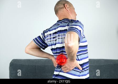 adult bald man stands, holds his back with his hand, a grimace of suffering on his face, the concept of problems with the spine, sciatica Stock Photo