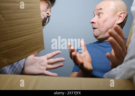 woman and a man opened a cardboard box with an ordered product, look into it, emotionally reacts to the contents, the concept of a postal item, a pack Stock Photo