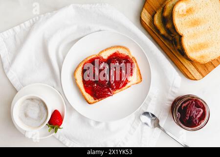 Breakfast with Toast and Strawberry Preserves and Cappuccino: Slice of toasted white bread and homemade berry preserves with coffee on white table Stock Photo
