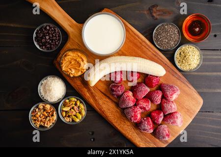 Strawberry Smoothie Bowl Ingredients on a Wooden Cutting Board: Frozen strawberries and banana with milk and various smoothy bowl toppings Stock Photo
