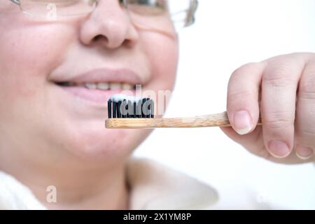 closeup female hand holding a wooden toothbrush, cleaning gel on black bristles for cleaning teeth, oral cavity care concept, daily routine of hygiene Stock Photo