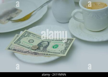 top view close-up on white plate with American dollars bills and coins, selective focus, cup of coffee, dishes with food, lunch concept in restaurant, Stock Photo