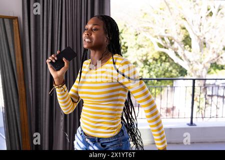 African American young woman indoors holding a smartphone, singing at home Stock Photo