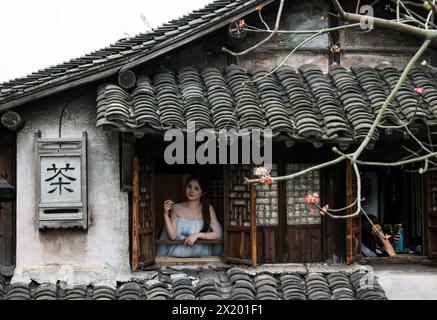 (240419) -- BEIJING, April 19, 2024 (Xinhua) -- A tourist looks outside at a tea house in the water town Wuzhen in Jiaxing City, east China's Zhejiang Province, April 11, 2024. Located in east China's Zhejiang Province, the waterside city Jiaxing is renowned for tourist destinations Nanhu Lake and Wuzhen. In the breezy month of April, the two tourist hotspots come alive with the gentle touch of spring. Nanhu Lake, with its shimmering waters and willow trees swaying along the lakeside, is a sight to behold. The historic water town Wuzhen also enchants with its emerald waters and whitewashed Stock Photo