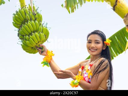 Hawaiian hula dancer offers a bunch of bananas growing on a palm tree Stock Photo