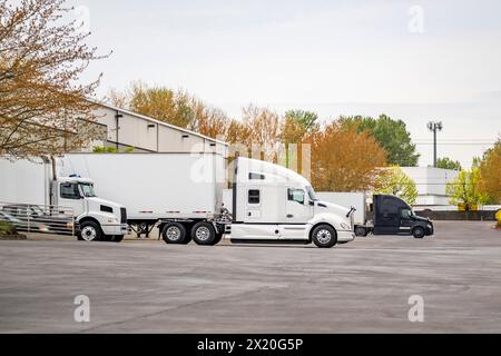 Industrial standard different bonnet long hauler big rig semi trucks with dry van semi trailers standing in the warehouse dock gates loading commercia Stock Photo