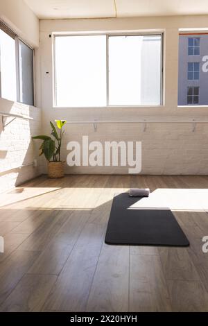 Sunlight fills yoga studio, highlighting empty black mat and rolled towel, copy space Stock Photo