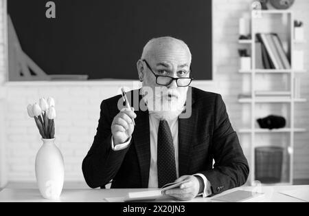 Teacher preparing for university exams. Professor holding a book and pointing. Teacher in college on university lecture. Stock Photo