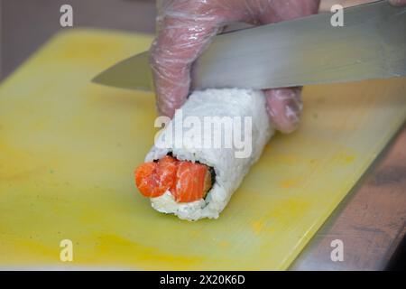 A gloved hand cuts sushi on a cutting board. Stock Photo