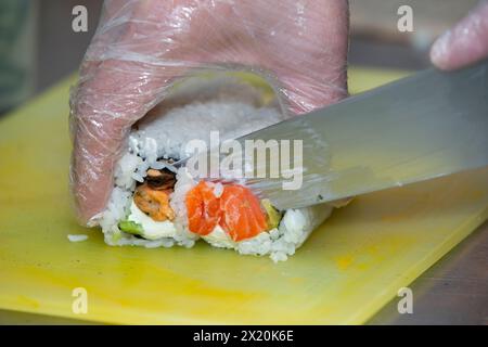 A gloved hand cuts sushi on a cutting board. Stock Photo