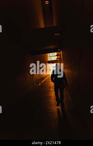 A man walks down a dark hallway with a light shining in front of him. The hallway is empty and the man is the only person in the scene. Scene is eerie Stock Photo