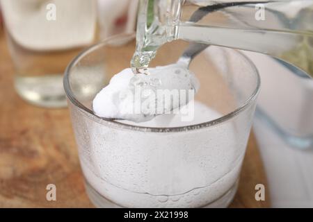 Pouring vinegar into spoon with baking soda over glass bowl at table, closeup Stock Photo