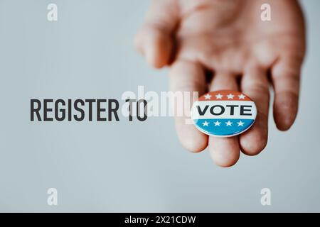 the text register to vote, with a vote badge in the hand of a man, on an off-white background Stock Photo