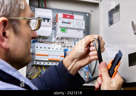 An electrician cuts TPE jacket of power cable using universal retractable utility knife. Stock Photo