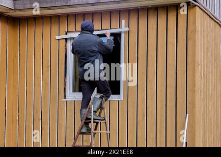 Exterior window finishing with metal jambs and mouldings, construction worker working standing on stepladder. Stock Photo