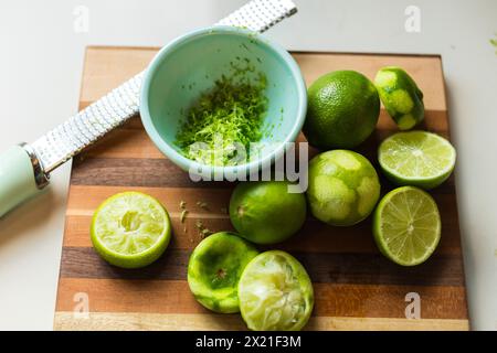 Zested and halved limes on a striped cutting board Stock Photo