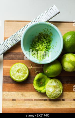 Zested and halved limes on a striped cutting board Stock Photo