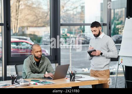 Two men deeply engrossed in their laptops, engaged in a collaborative coding session at a modern office table, diversity and inclusion Stock Photo