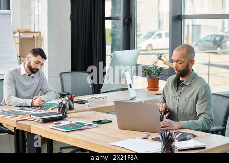 Two businessmen sit at a table, immersed in their laptops, brainstorming and collaborating on a project in a modern office setting, inclusive Stock Photo